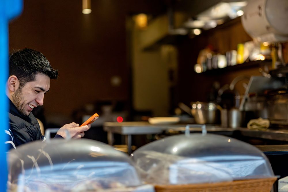Dueño de una cafetería revisando mensajes de clientes en el móvil
